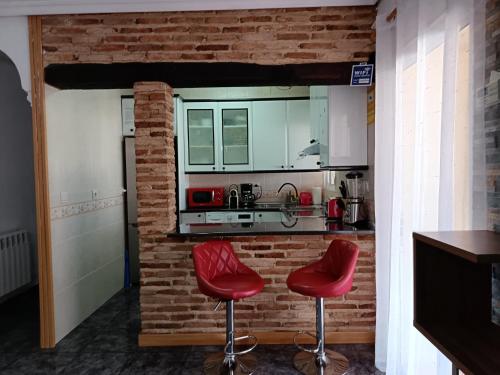 a kitchen with two red bar stools and a brick wall at Casa Oasis Puertollano, una casa rural en Puertollano, agradable, con Piscina en zona tranquila in Puertollano