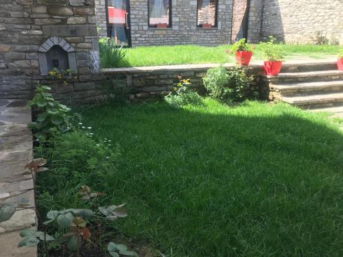 a yard with green grass and a stone wall at Gogo Moustache Guest House in Përmet