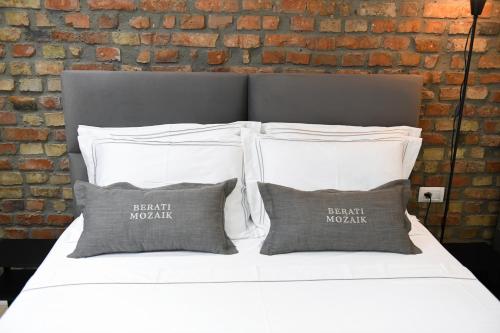 a white bed with three pillows and a brick wall at Berati Mozaik Hotel in Berat