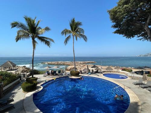a pool at a resort with palm trees and the ocean at Ocean Front, 3 bedroom, 3 bathroom, Casa Natalia, Playa Esmeralda in Puerto Vallarta