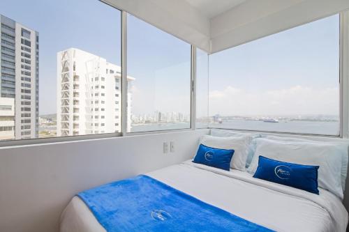 a white bed with blue pillows in a room with windows at Vista de lujo al mar y la bahía in Cartagena de Indias
