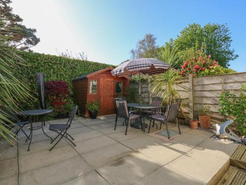 a patio with a table and chairs and an umbrella at Hafan Bach - 233 Cae Du in Abersoch