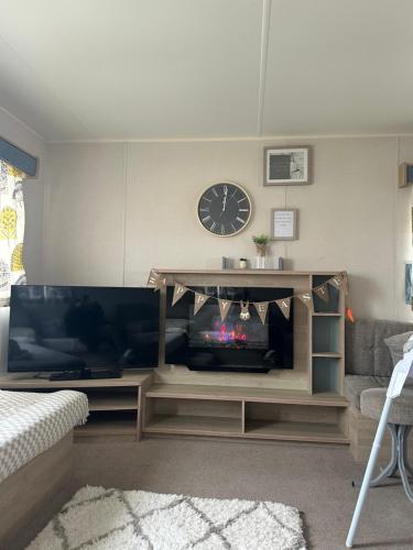 a living room with a television and a clock on the wall at The Aurora van at Presthaven sands holiday park and beach resort in North Wales- 8 berth in Prestatyn