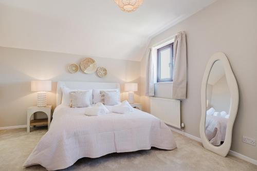 a white bedroom with a large bed with a mirror at Beautiful 4 Bedroom Cotswolds Home near Woodstock! in Wootton