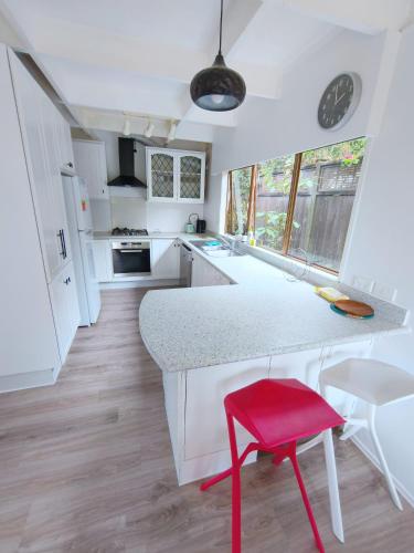a kitchen with a counter and a red stool at Spa Retreat Spacious 7 BRS 3 Baths Movie Lounge nice Garden with Parking in Auckland