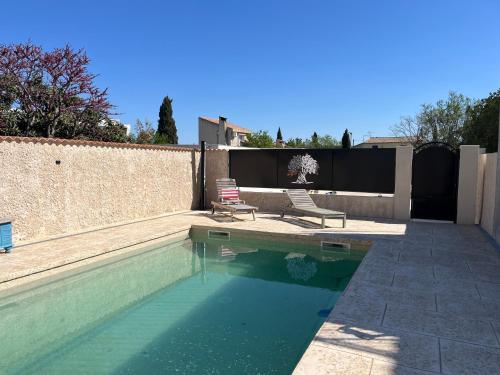 - une piscine avec 2 chaises à côté d'un mur dans l'établissement Haut de villa avec piscine privée et extérieur, à Lançon-Provence
