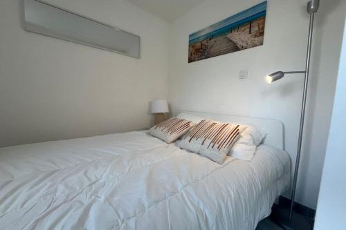 un lit blanc avec deux oreillers dessus dans l'établissement Appartement Jardin Piscine Proche de la mer, à Narbonne