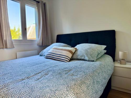 - un lit avec une couette et des oreillers bleus ainsi qu'une fenêtre dans l'établissement Le Yearling, à Deauville