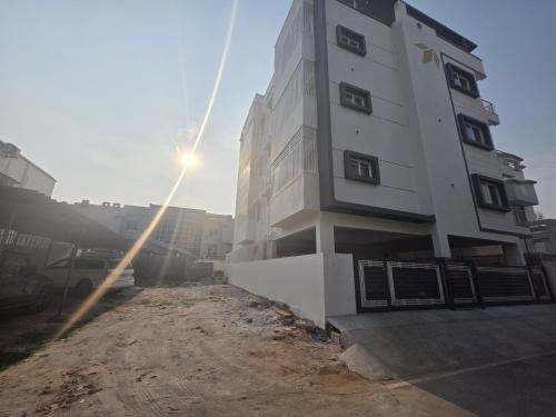 a tall white building with the sun shining behind it at Blossom Service Apartment in Mysore