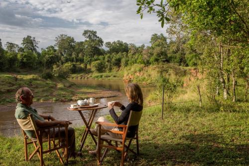 a man and woman sitting at a table by a river at Sentinel Mara Camp in Talek