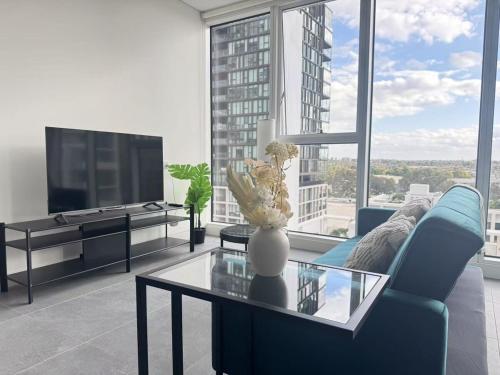 a living room with a blue couch and a glass table at New Apartment in Olympic Park with Pool and Gym in Sydney