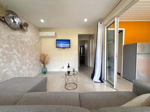 een woonkamer met een bank en een tv aan de muur bij Hana Mana Bungalow - Plage proche, Grande Terrasse in Grand-Bourg