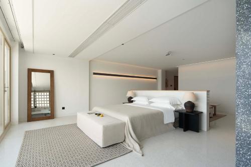 a white bedroom with a bed and a stool at Shenzhen GuanHu Secret Wild Reef Seaview Hotel in Shenzhen