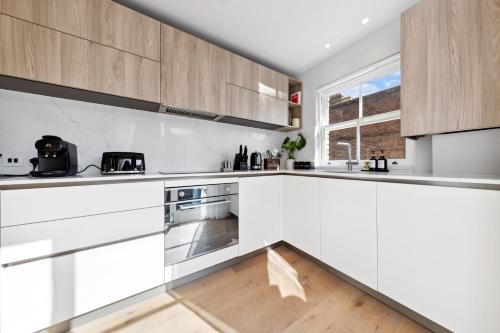 a white kitchen with wooden cabinets and a window at The Notting Hill Villa in London