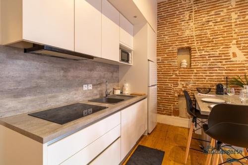 Il comprend une cuisine avec un évier, une table et un mur en briques. dans l'établissement Leon - Capitole - Hypercentre Ville - Métro, à Toulouse