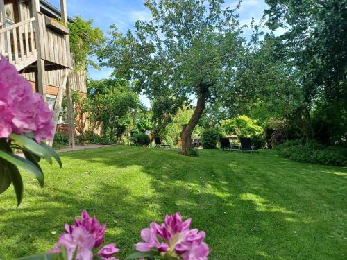 a green yard with pink flowers and a tree at Ferienhof Landfrieden in Vollerwiek