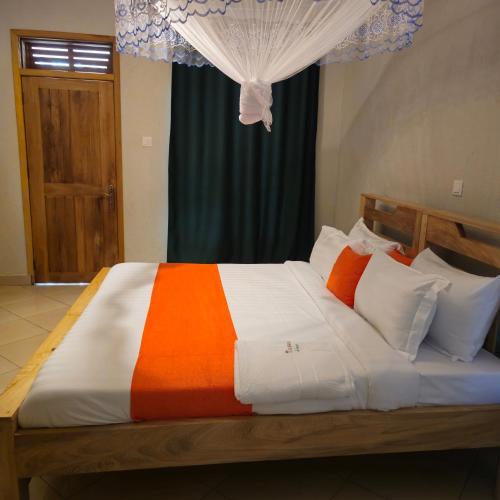 a bedroom with a large bed with an orange and white blanket at Tusubira village in Jinja