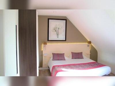 a bedroom with a bed with two pink pillows at The Originals Boutique, Hôtel Les Quatre Salines, Le Mont Saint-Michel Sud in Roz-sur-Couesnon