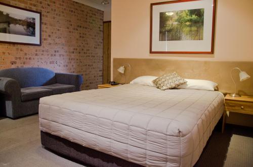 a bedroom with a large bed and a chair at Baybrook Motor Inn in Muswellbrook
