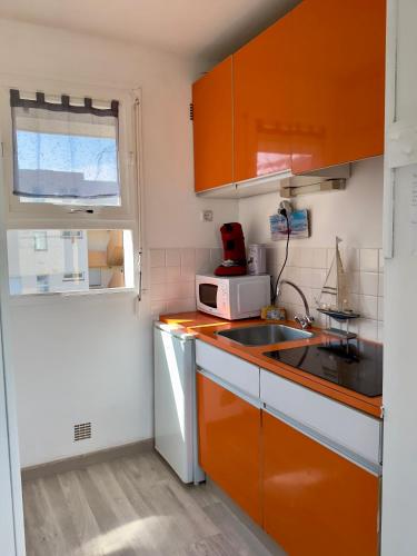 une petite cuisine avec des armoires orange et un évier dans l'établissement Le bord 2 mer - Draps et ménage inclus, au Barcarès