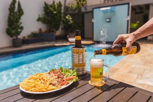 a person pouring a beer into a glass next to a plate of food at Hotel Nacional Inn Araçatuba in Araçatuba