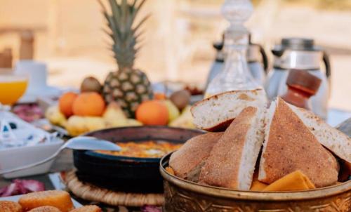 a table topped with a basket of bread and fruit at Excellent Luxury Camp in Merzouga