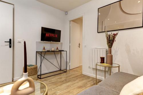 un salon avec un canapé et une télévision au mur dans l'établissement Charme Parisien pres des Buttes-Chaumont, à Paris