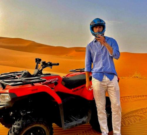 a man standing next to a red atv in the desert at Excellent Luxury Camp in Merzouga