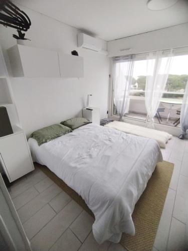 a white bedroom with a large bed and a window at Petit cocon baigné de lumière in Le Grau-du-Roi