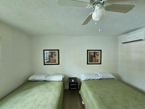 two beds in a room with a ceiling fan at Diamante Lakes Condominium, in front of Arena GNP in Acapulco