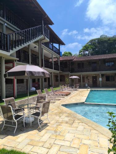 a pool with chairs and an umbrella next to a building at Pousada Margerie Ubatuba - Ítagua in Ubatuba