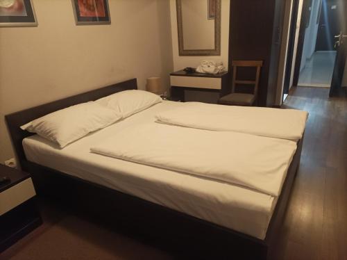a bedroom with a bed with white sheets and a table at Hotel Storia in Čapljina