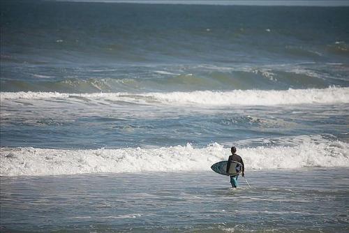 a man walking into the ocean with a surfboard at 404 - 2/2 Ocean View Escape in New Smyrna Beach
