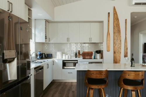 a kitchen with white cabinets and wooden bar stools at The Boat House Retreat Squeaking Point in Port Sorell