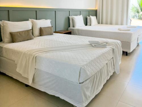 two beds in a hotel room with white sheets at Hotel Premium Recanto da Passagem in Cabo Frio