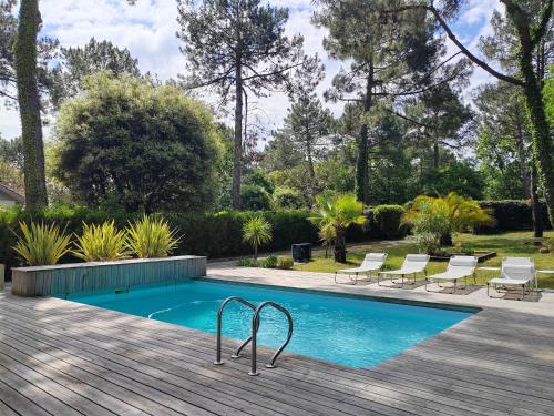 une piscine avec des chaises et une terrasse en bois dans l'établissement Le Bordelou, 6-8 pers, heated pool, à Lacanau-Océan