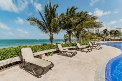 a row of chairs by a swimming pool next to the ocean at MAREA New 2 BDR Beachfront by Casa Paraíso in Cancún