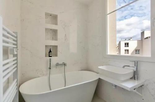 La salle de bains est pourvue de 2 lavabos, d'une baignoire et d'une fenêtre. dans l'établissement Appartement 2 pieces Boulogne-Billancourt, à Boulogne-Billancourt