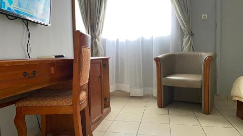 a desk and a chair in a room with a window at Hotel Peninsule Bonamoussadi Douala in Douala