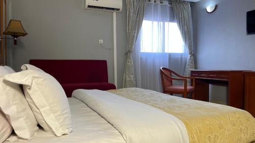 a hotel room with a bed and a desk and a window at Hotel Peninsule Bonamoussadi Douala in Douala