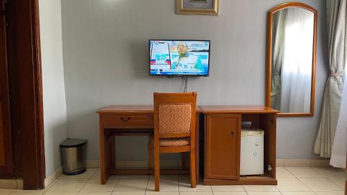 a room with a desk and a television on a wall at Hotel Peninsule Bonamoussadi Douala in Douala
