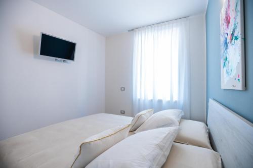 a white bedroom with a bed and a tv at ES Rooms and Apartments in Nago-Torbole
