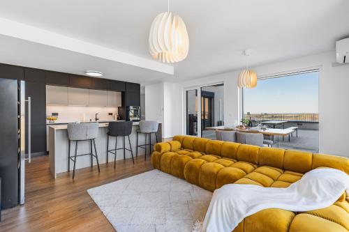 a living room with a yellow couch and a kitchen at BNB Panorama Bory Penthouse in Bratislava