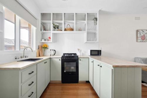 Geelong WestにあるCosy Townhouse in the Heart of Geelong Westのキッチン(白いキャビネット、黒いコンロ付)
