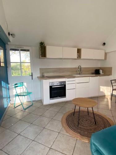 une cuisine avec des armoires blanches et une table et une chaise dans l'établissement Petit gîte au coeur du haras, à Le Breuil-en-Auge