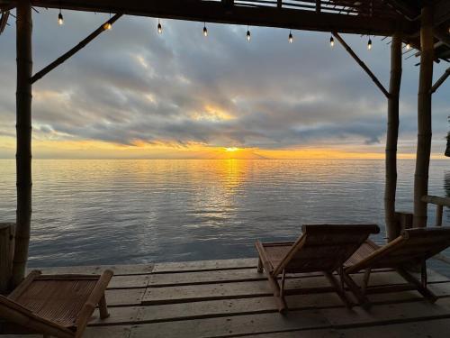 a sunset over the water with two chairs on a dock at Wanderlust Resort Samal in Del Monte