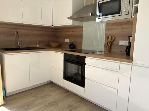 une cuisine avec des armoires blanches et un four noir dans l'établissement Appartement T2 avec Cabine, Terrasse et Climatisation à Saint Pierre la Mer - FR-1-229D-156, à Fleury