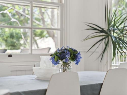 a white table with a vase of blue flowers on it at Jacaranda Villa Korora Beach NSW in Kororo Basin