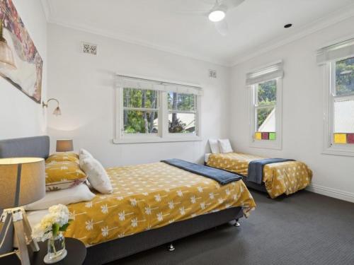 two beds in a room with white walls and windows at Jacaranda Villa Korora Beach NSW in Kororo Basin