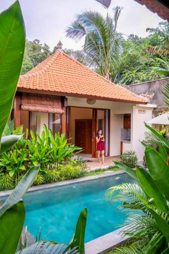 a woman standing in front of a house with a swimming pool at Cempaka Kembar Ubud in Ubud